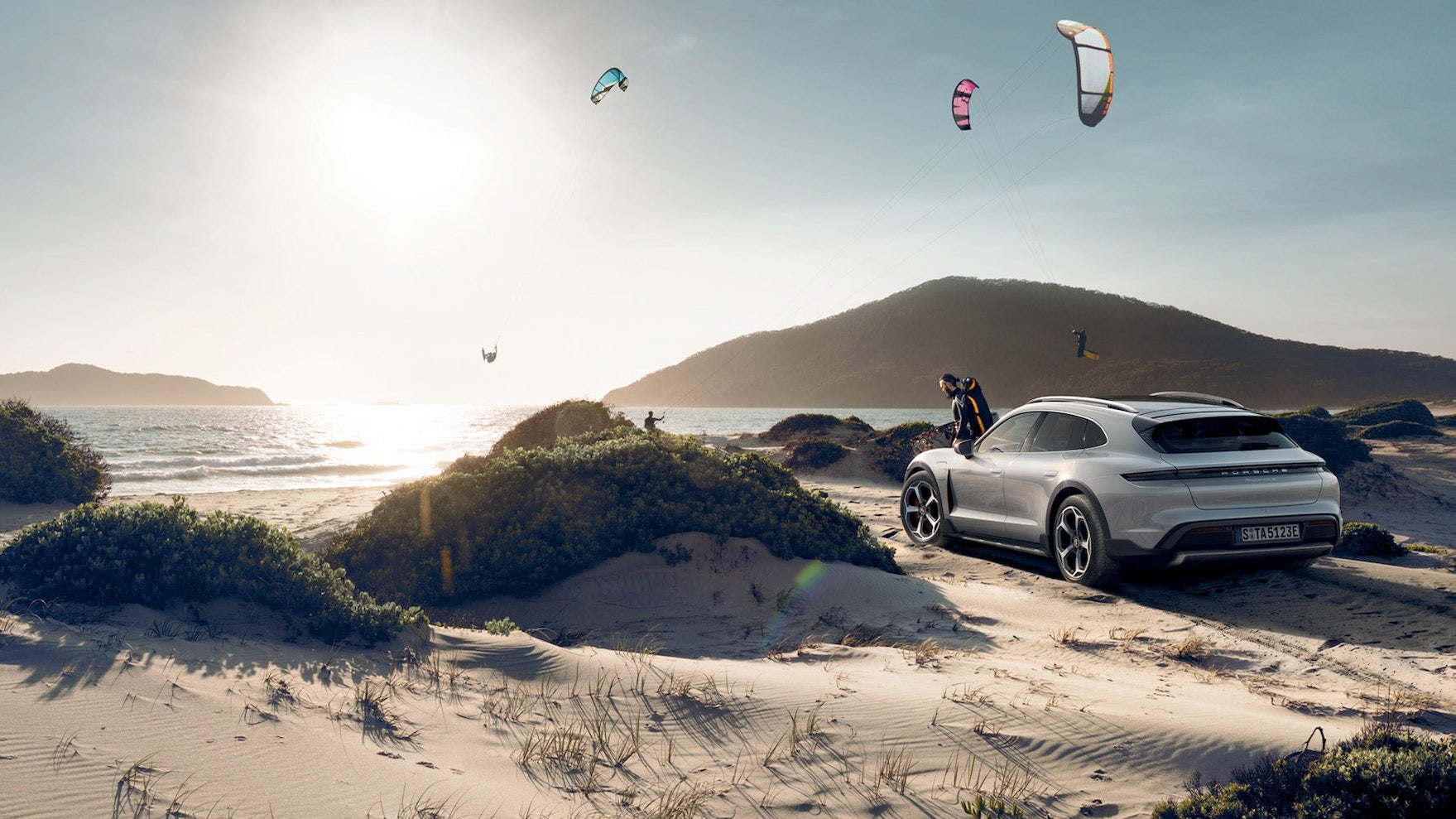 2024 Porsche Taycan Turbo S Cross Turismo parked on the beach with paragliders overhead